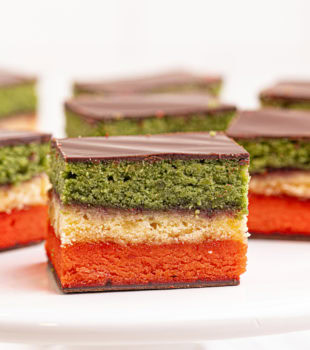 an Italian rainbow cookie on a small white pedestal with more cookies behind