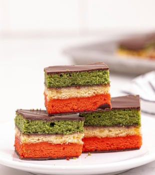 an Italian rainbow cookie on top of two more cookies on a white plate