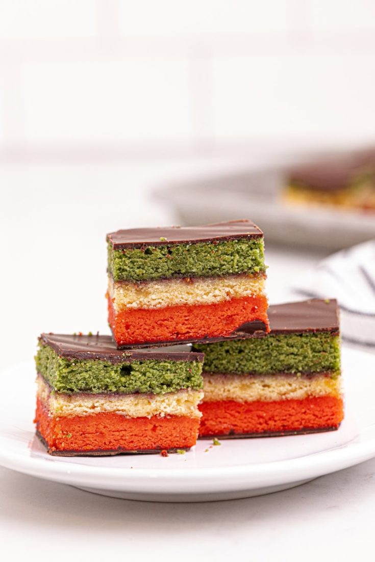 an Italian rainbow cookie on top of two more cookies on a white plate