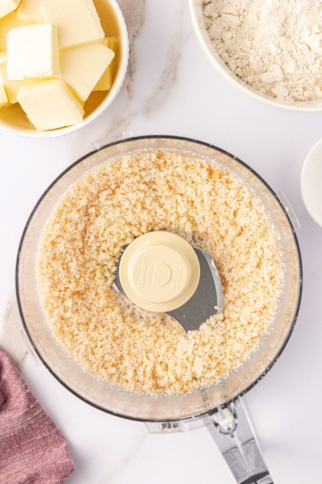 overhead view of ground macadamias and sugar in the bowl of a food processor