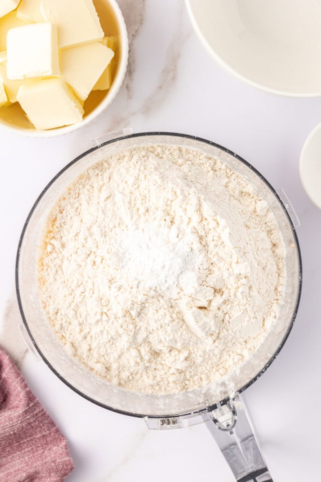 overhead view of flour and baking powder added to ground macadamias and sugar in the bowl of a food processor