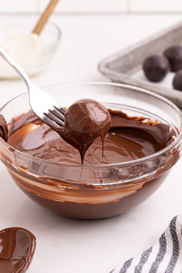 an Oreo truffle being dipped into melted dark chocolate