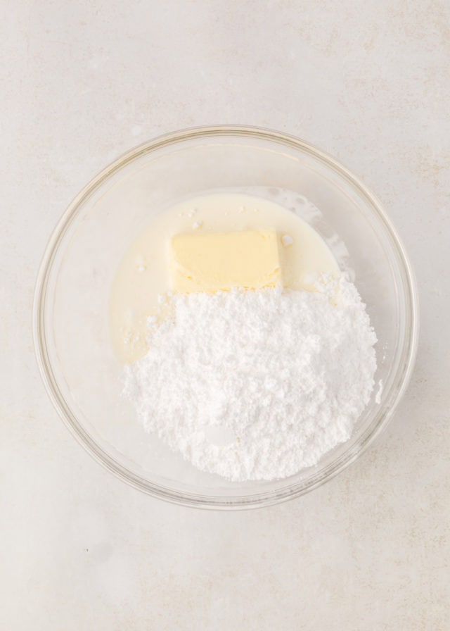 overhead view of confectioners' sugar, butter, cream, and peppermint extract in a mixing bowl