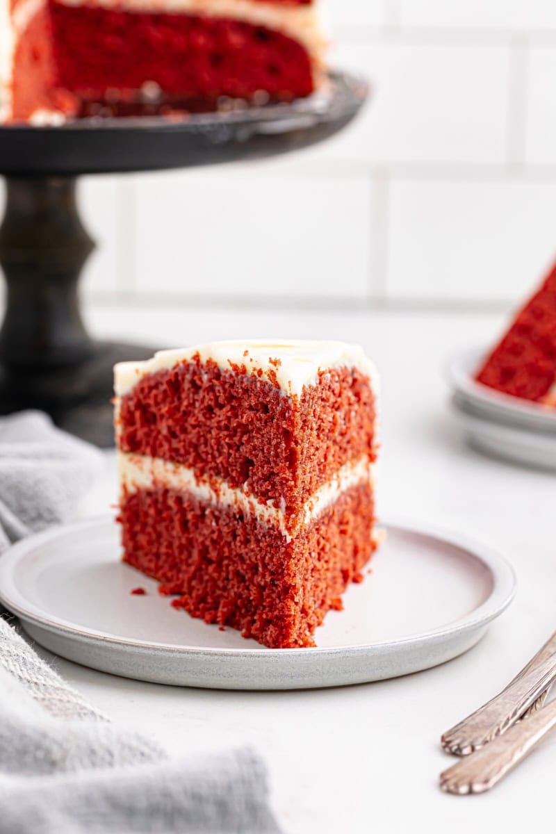 a slice of red velvet cake on a white plate with remaining cake in the background