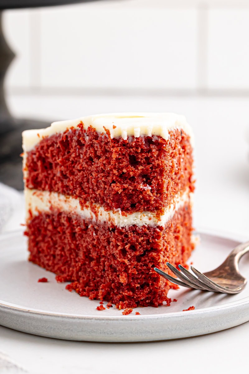 a slice of red velvet cake on a white plate with a bite missing