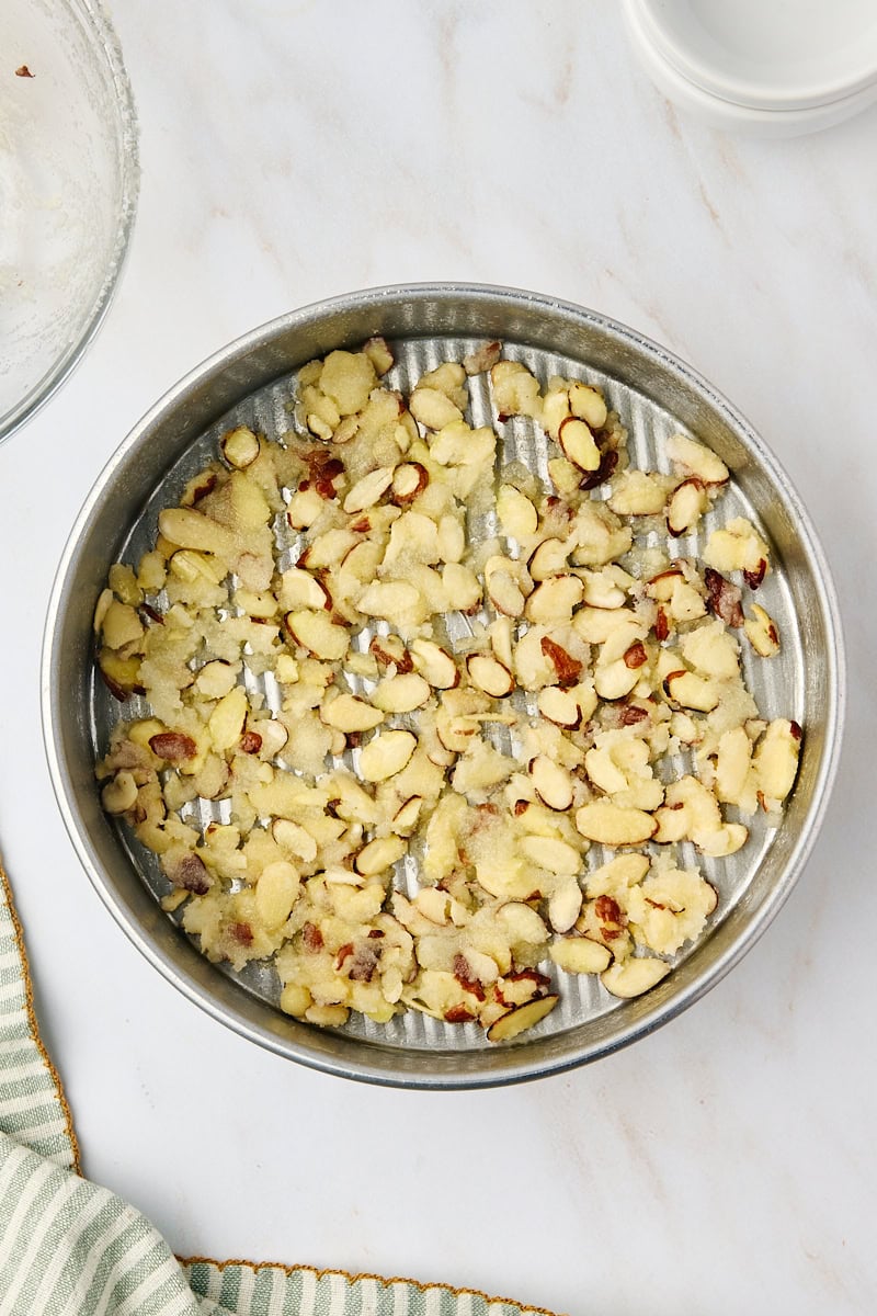 An overhead shot showing the almond topping mixture spread evenly across the bottom of a greased round cake pan.