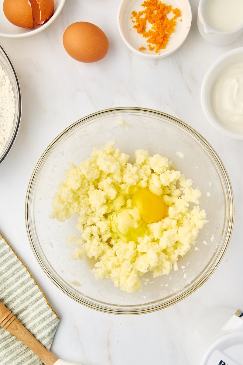 A large egg being cracked and added to the creamed butter and sugar mixture in a mixing bowl, illustrating the process of adding eggs one at a time.