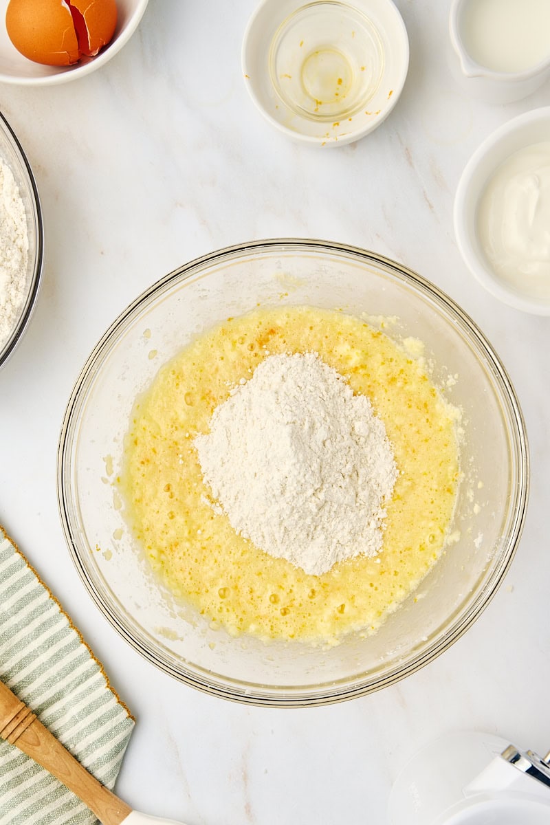 Overhead view of dry ingredients being added in portions to the wet cake batter mixture.