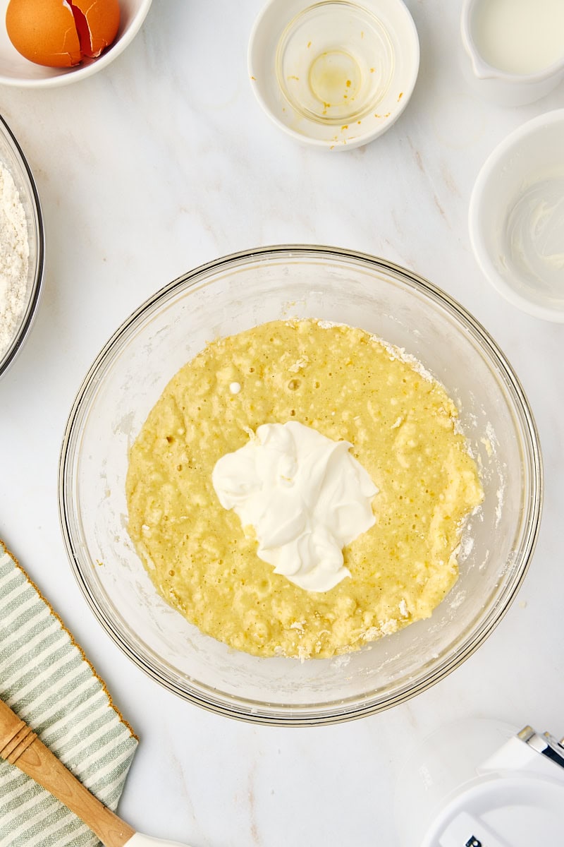 Overhead view of sour cream being added to the cardamom cake batter, illustrating the alternating process of wet and dry ingredient additions.