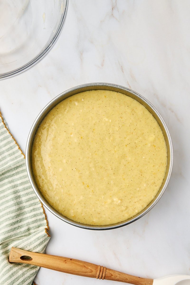 Overhead view of the cardamom cake batter smoothly spread over the almond topping in the cake pan, perfectly ready for the oven.