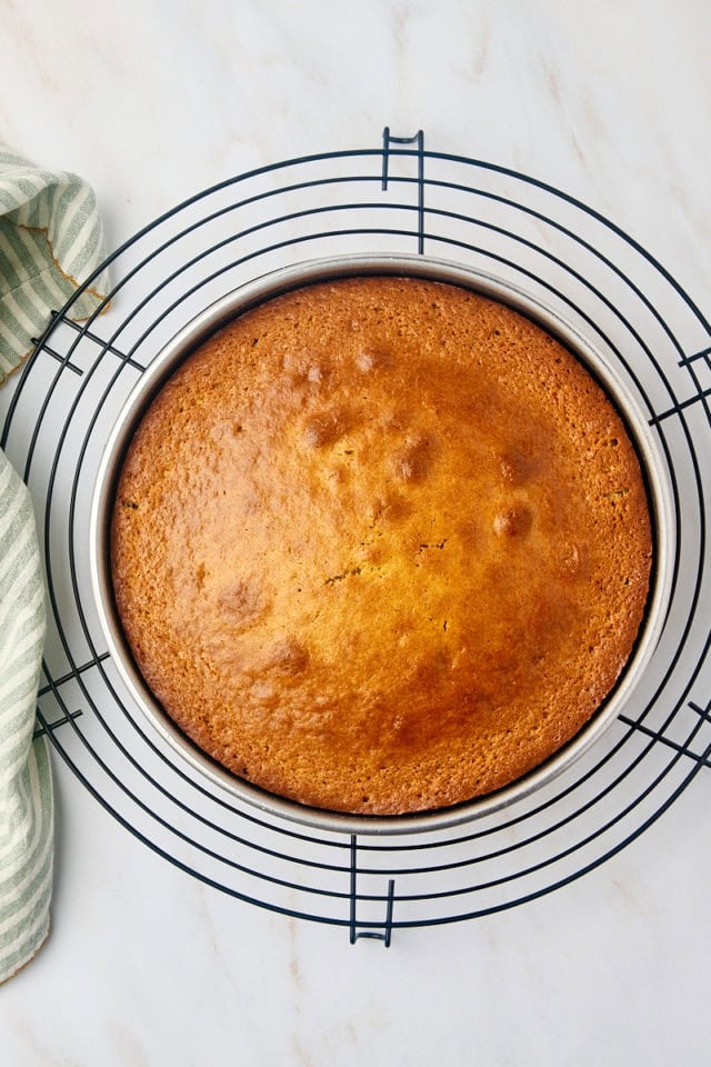 overhead view of freshly baked cardamom cake in a cake pan on a wire rack