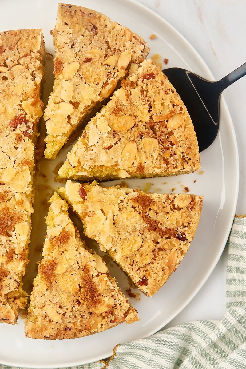 overhead view of partially sliced cardamom cake with a slice on a cake server