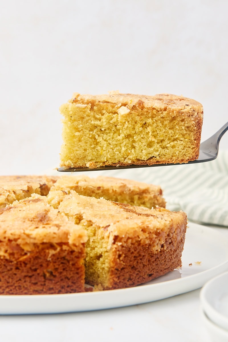 a slice of cardamom cake on a cake server being lifted away from the remaining cake