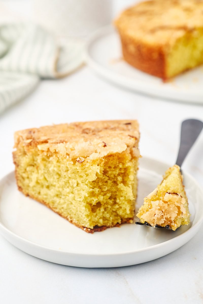 a slice of cardamom cake on a white plate with a bite on a fork