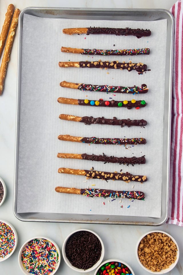 overhead view of chocolate covered pretzel rods on a parchment-lined baking sheet to set