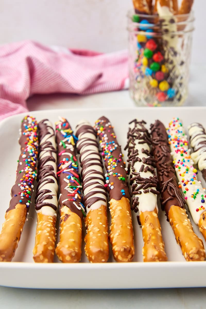 chocolate covered pretzel rods on a white tray with more in a jar in the background