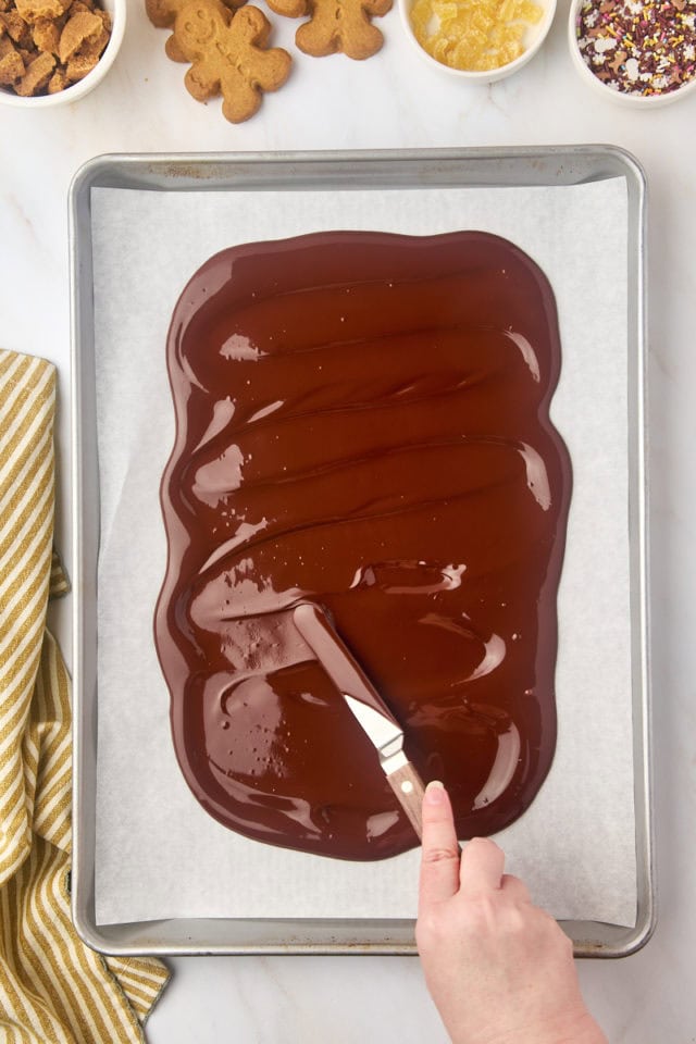 overhead view of melted chocolate being spread in a thin layer on a parchment-lined baking sheet