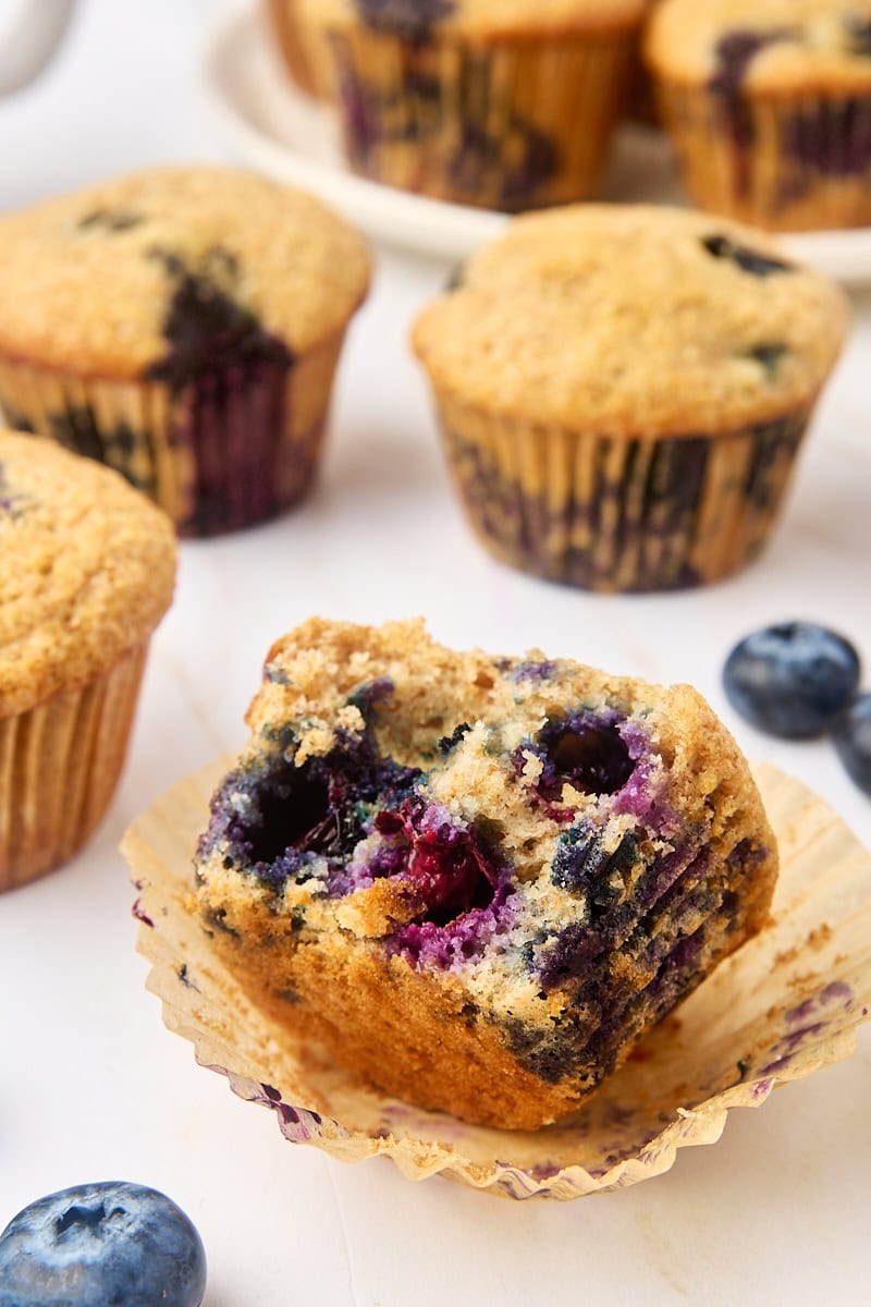 a whole wheat blueberry muffin with a bite missing, surrounded by more muffins