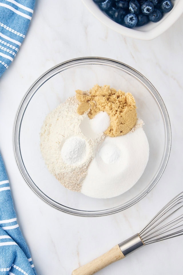 overhead view of whole wheat flour, all-purpose flour, sugar, brown sugar, baking powder, baking soda, and salt in a glass mixing bowl