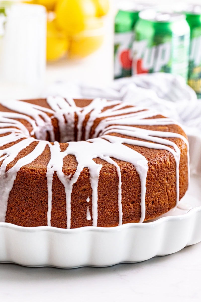 glazed 7UP cake on a white cake plate with lemons and cans of 7UP in the background