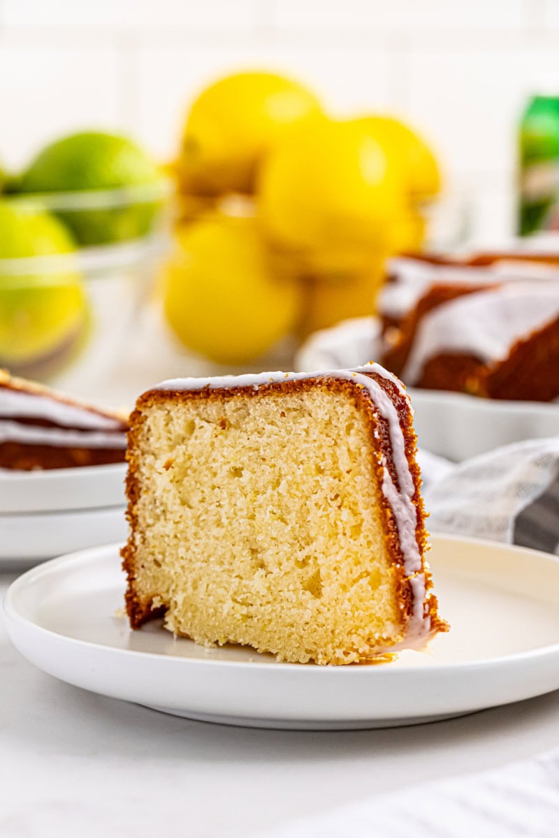 a slice of 7UP cake on a white plate with lemons and limes in the background