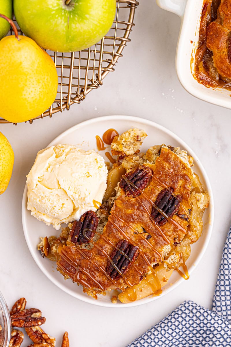 overhead view of a serving of caramel apple pear cobbler on a white plate with a scoop of ice cream