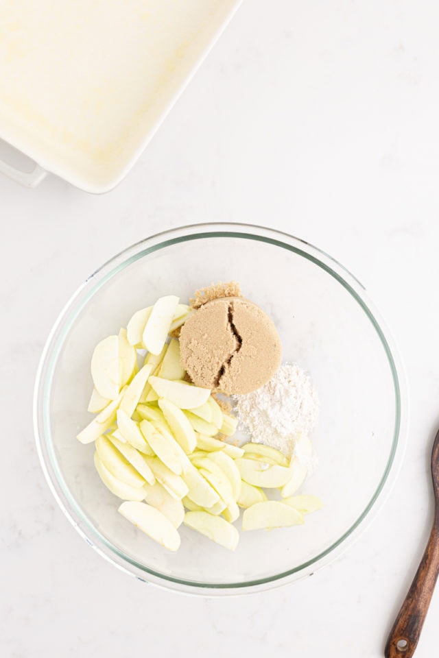 overhead view of apples, flour, and brown sugar in a glass bowl