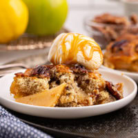 a serving of caramel apple pear cobbler topped with ice cream and caramel sauce