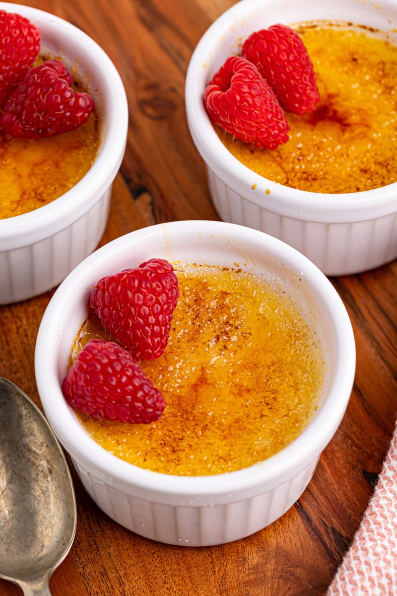 three ramekins of crème brûlée topped with raspberries