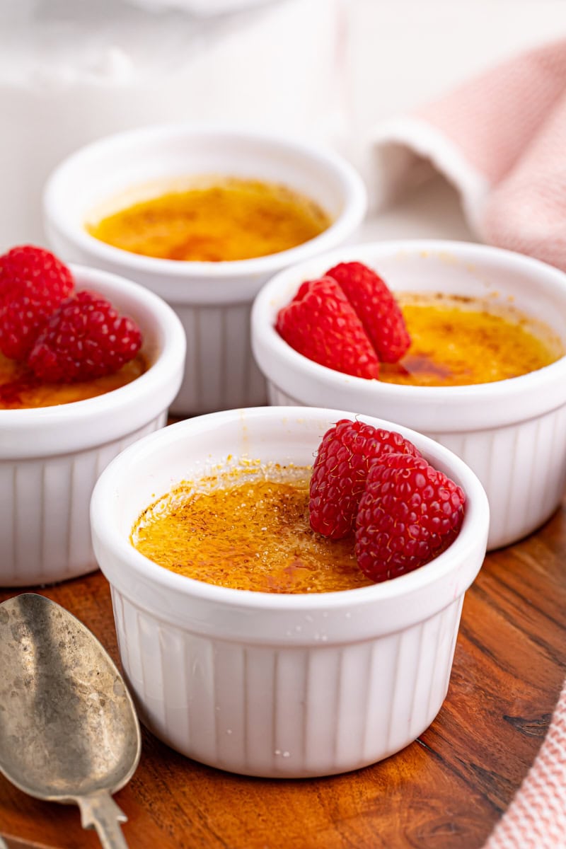 four ramekins of crème brûlée on a wooden serving board