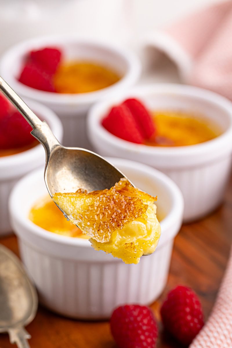 a spoonful of crème brûlée with ramekins of crème brûlée in the background