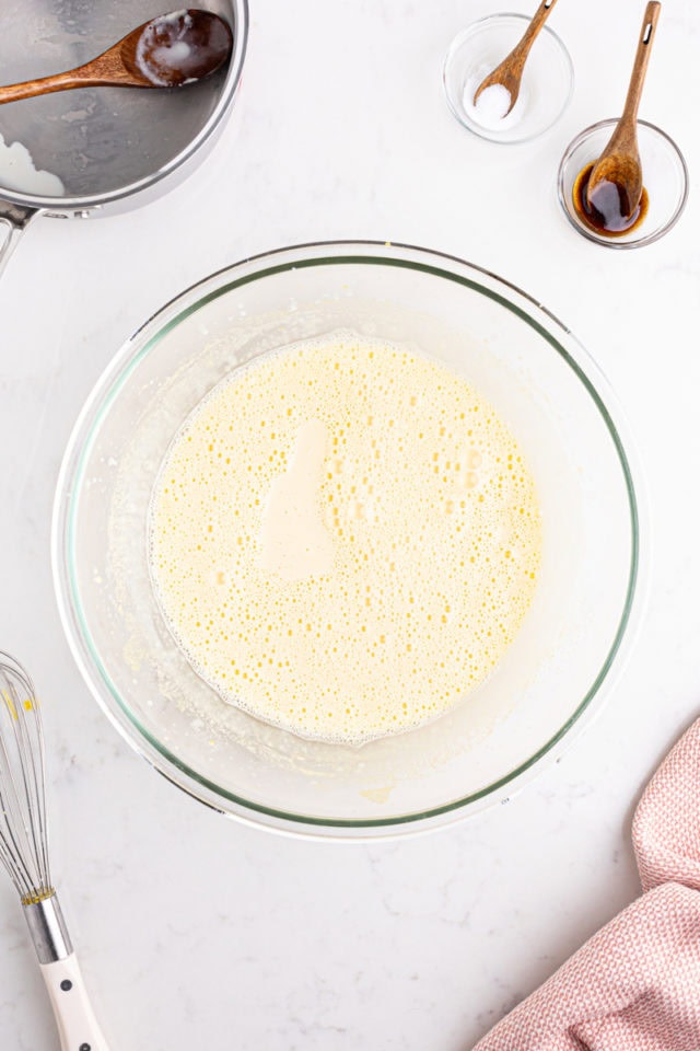 overhead view of heated cream poured over beaten egg yolks and sugar