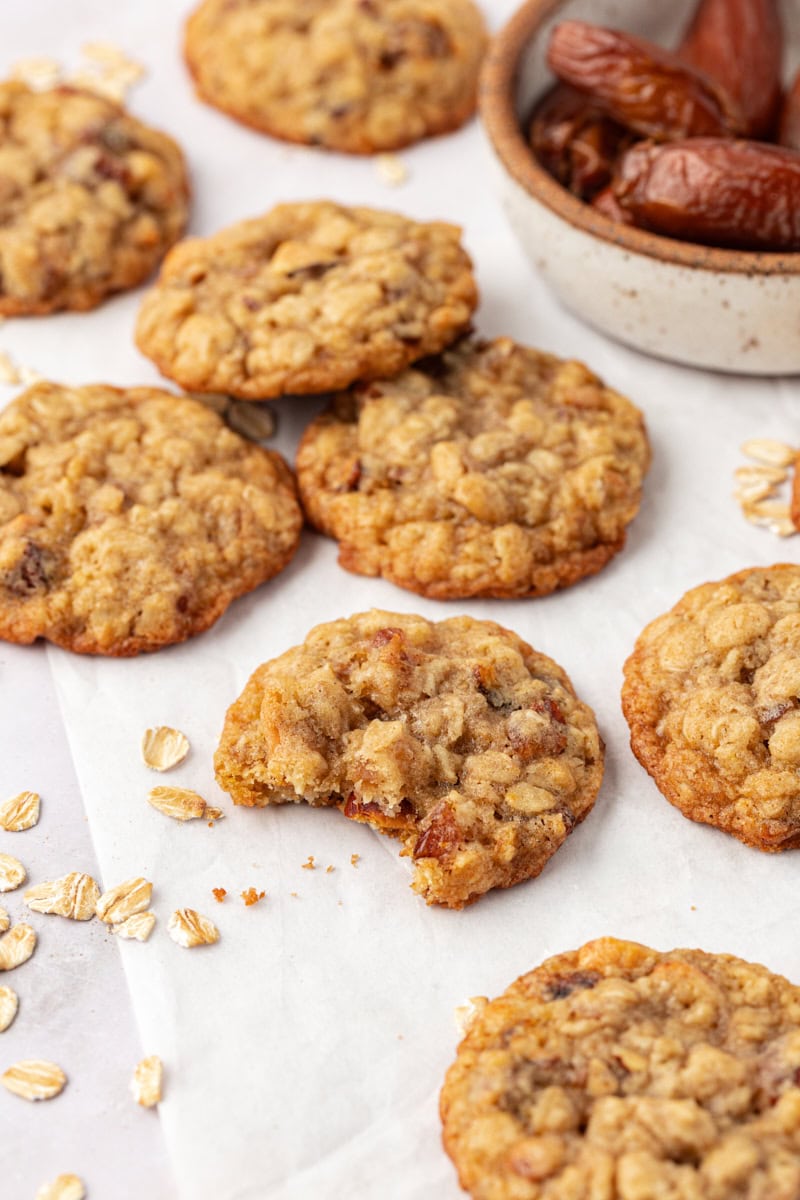 several oatmeal date cookies on parchment paper, with a bite missing from one of the cookies