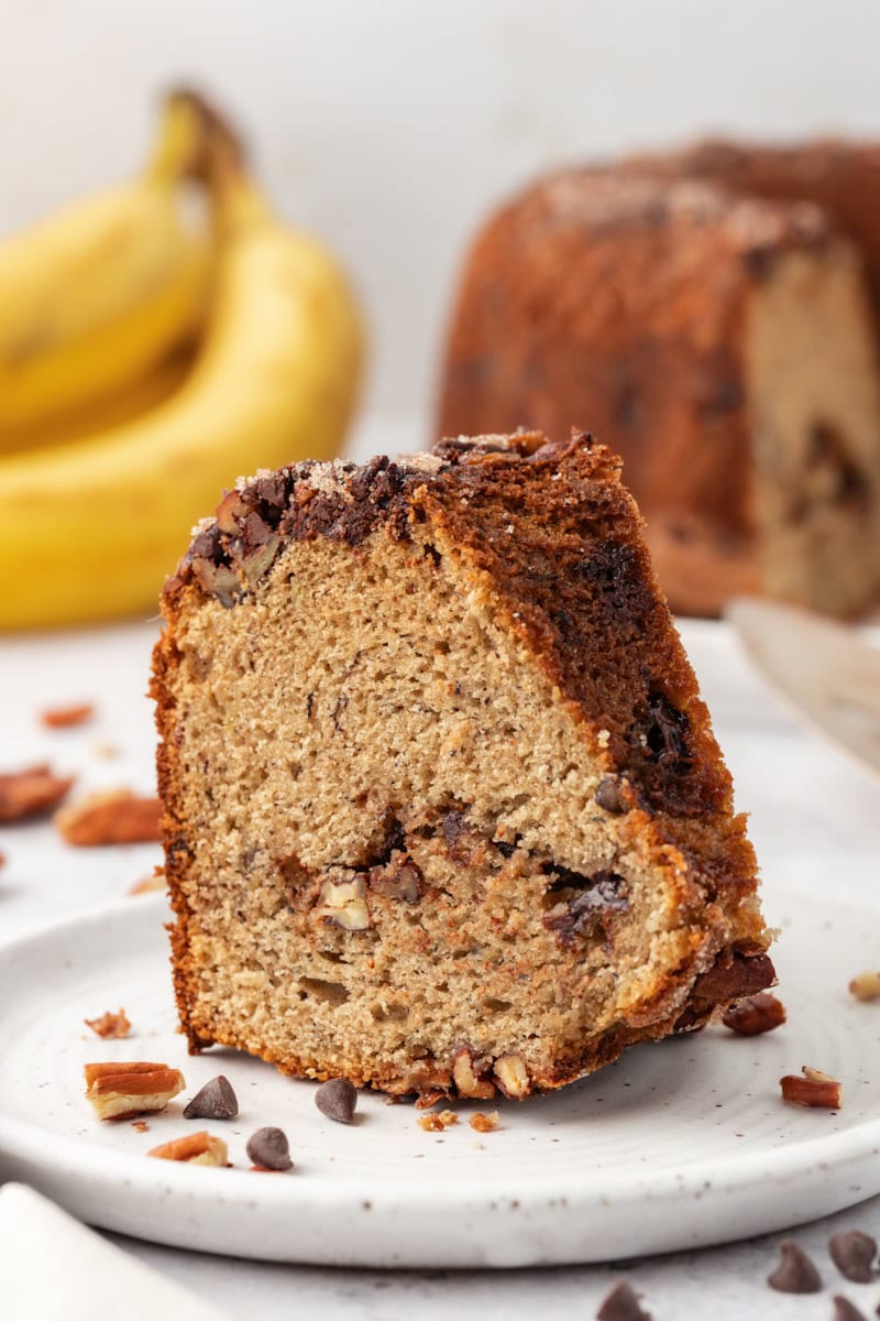 a slice of banana coffee cake on a white plate with more cake in the background