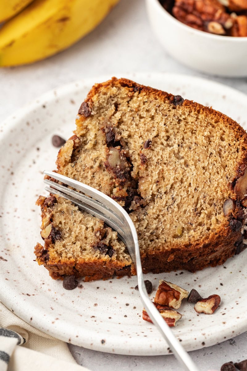 a fork cutting into a slice of banana coffee cake on a white plate