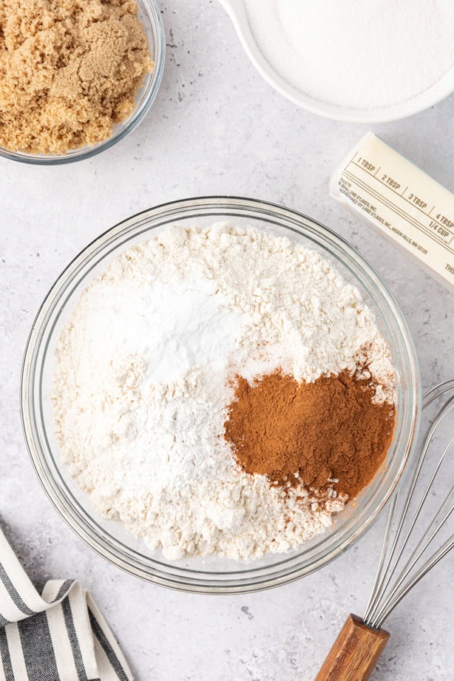 overhead view of flour, baking powder, baking soda, cinnamon, and salt in a glass mixing bowl