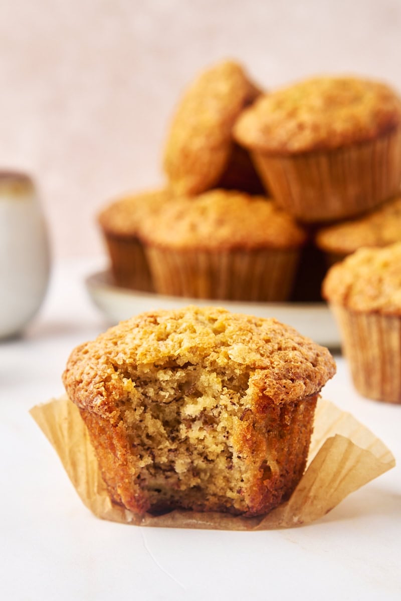 a banana muffin with a bite missing; more muffins on a plate in the background