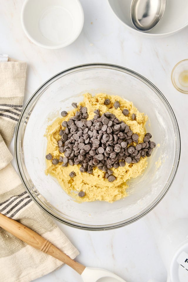 overhead view of chocolate chips added to cookie dough in a glass mixing bowl