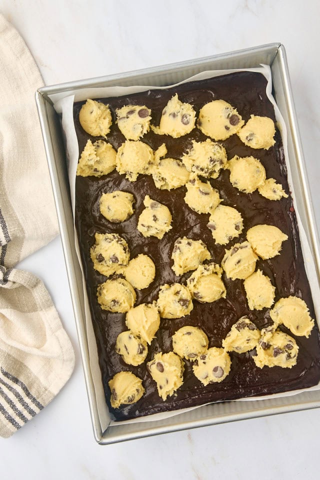 overhead view of chocolate chip cookie dough dropped by spoonfuls onto brownie batter in a 9x13 pan