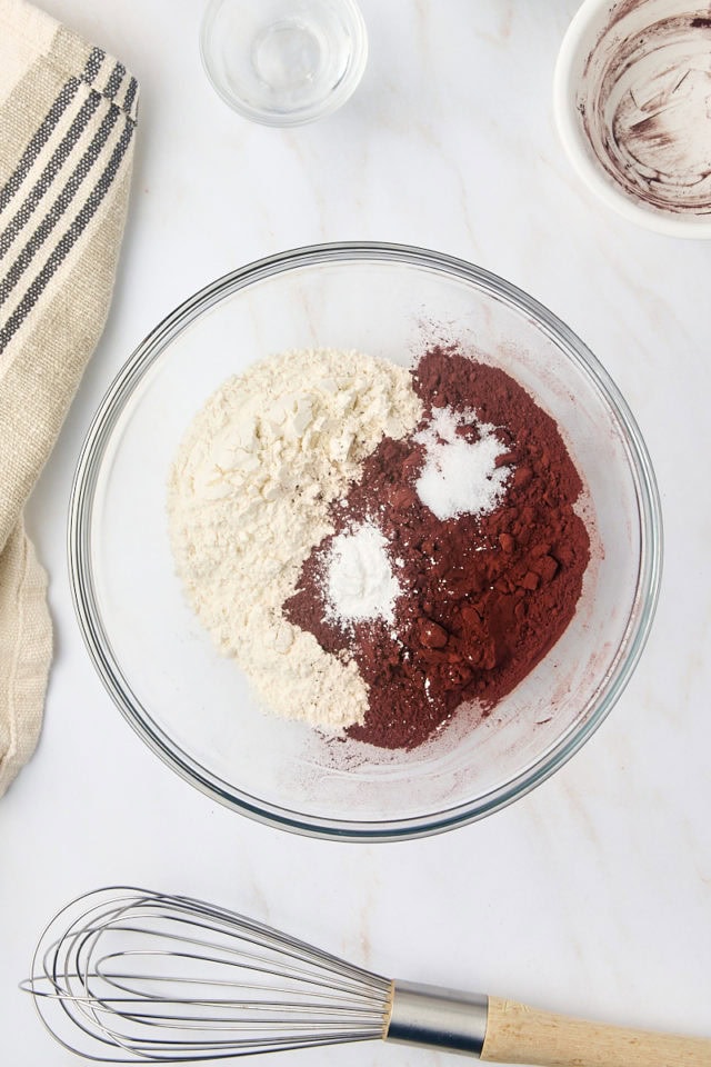 overhead view of cocoa powder, flour, baking powder, and salt in a glass mixing bowl