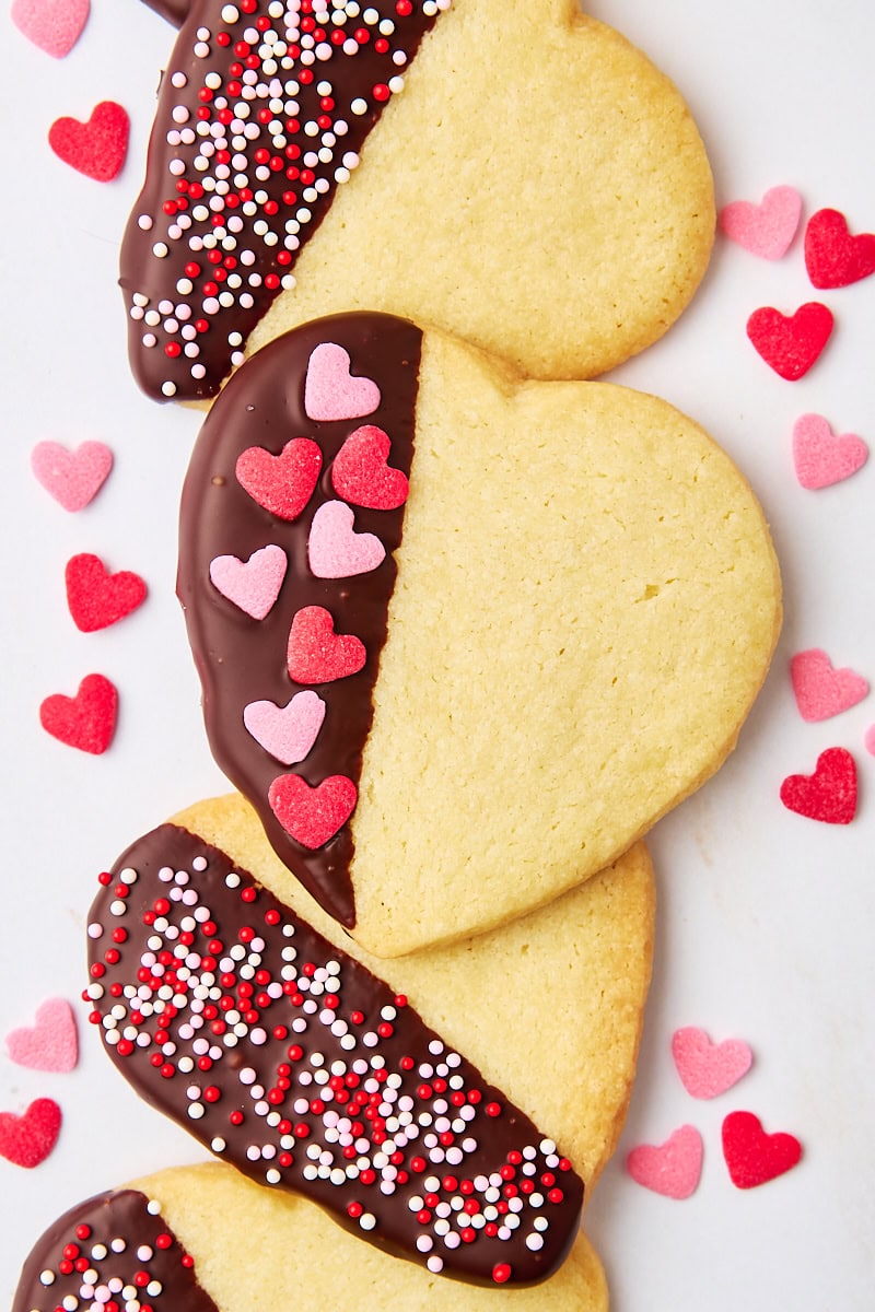 overhead view of four chocolate-dipped shortbread cookies surrounded by heart-shaped sprinkles