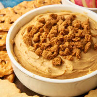 cookie butter dip in a white bowl surrounded by shortbread, pretzels, and apple slices