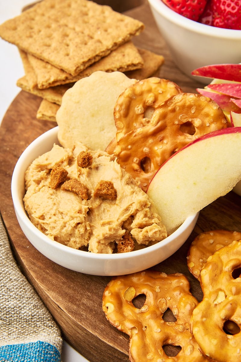 a serving of cookie butter dip in a small bowl with pretzels, shortbread, and an apple slice