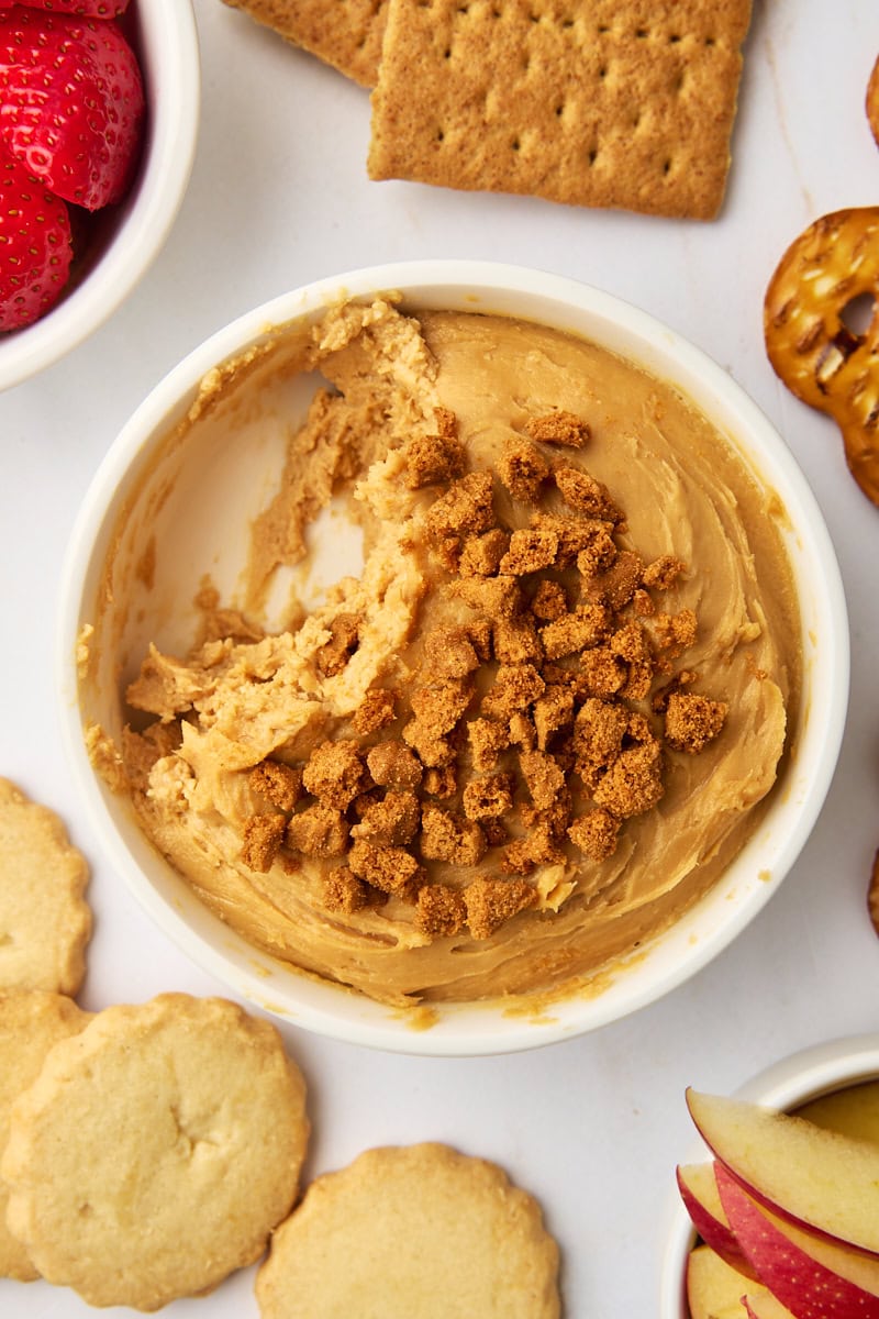 a bowl of cookie butter dip with a few servings missing, surrounded by various dippers