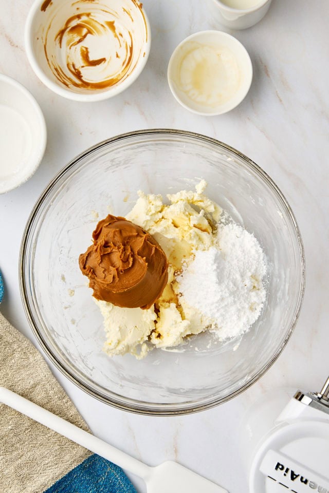 overhead view of cookie butter, confectioners' sugar, and vanilla added to beaten cream cheese in a glass mixing bowl