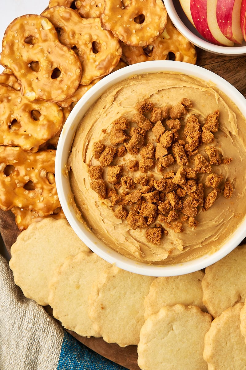 overhead view of cookie butter dip in a bowl surrounded by pretzels, shortbread, and apple slices