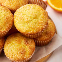 pile of orange ricotta muffins on a parchment-covered wooden plate