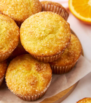 pile of orange ricotta muffins on a parchment-covered wooden plate