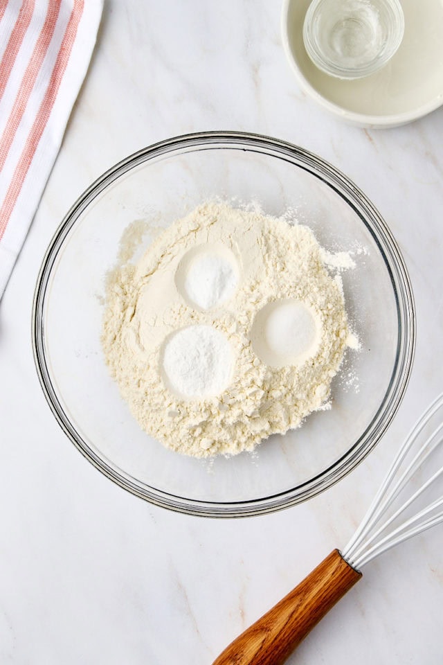 overhead view of flour, baking powder, baking soda, and salt in a glass mixing bowl