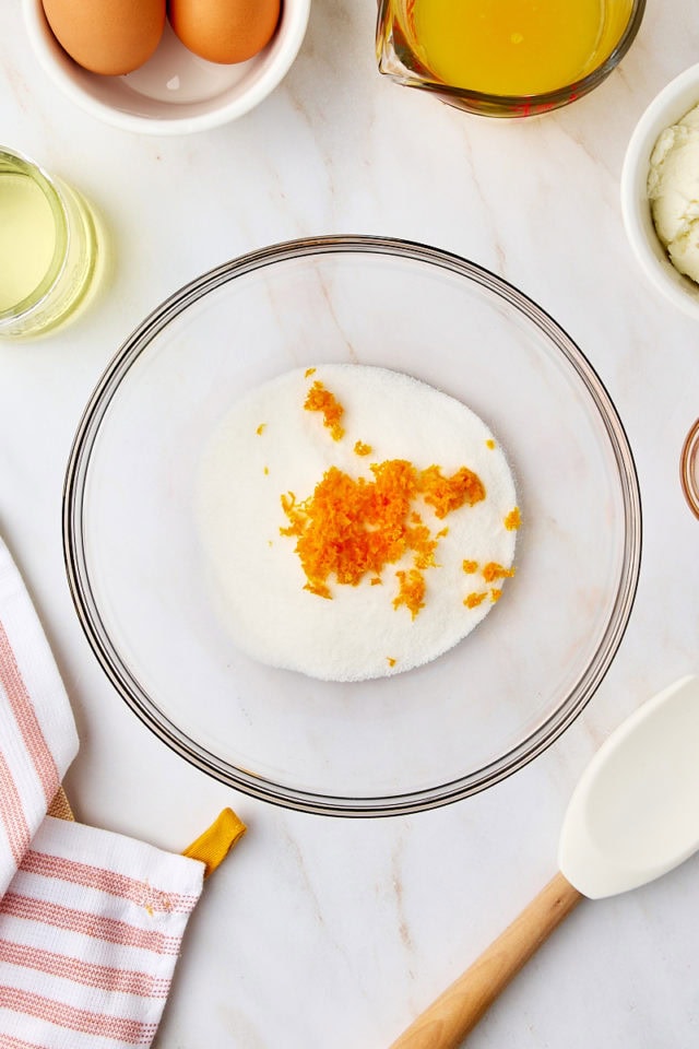 overhead view of sugar and orange zest in a glass mixing bowl